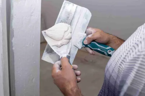Application d'enduit de lissage sur un mur. Le temps de séchage est crucial avant le ponçage pour un fini parfait.