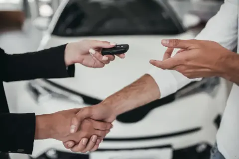 Wręczenie kluczyków do pierwszego auta. Uścisk dłoni na tle nowego samochodu.