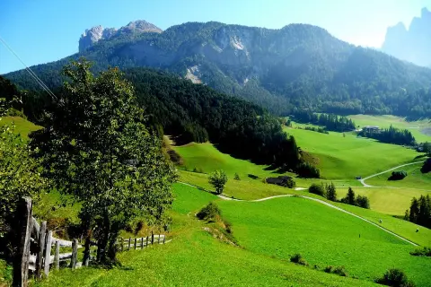Verdi colline e montagne maestose incorniciano i pittoreschi paesi del Val di Funes, con un sentiero che serpeggia tra prati lussureggianti.