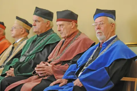 Czterech mężczyzn w togach akademickich i czapkach rektora siedzi w rzędzie.