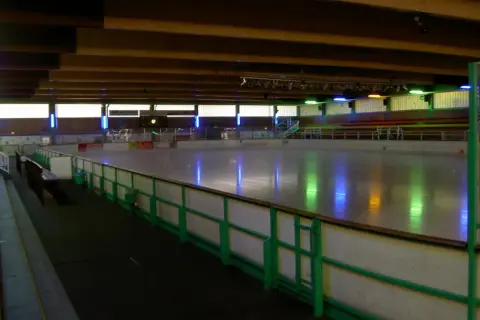 Leere Eisfläche in der Eissporthalle Bergisch Gladbach, beleuchtet von bunten Lichtern.