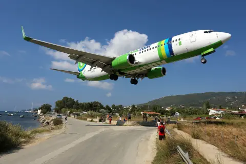 Ett flygplan landar lågt över vägen vid Skiathos flygplats. Människor står längs vägen och tittar upp.