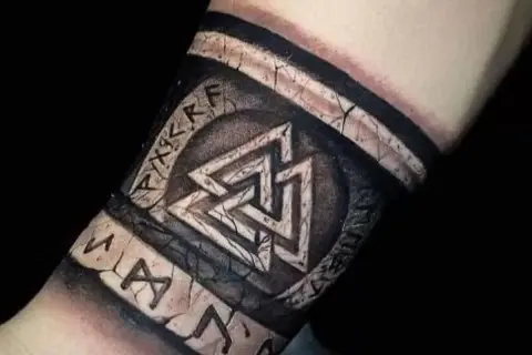Tatuaże wikingów na przedramieniu: symbol Walhalla i runy, wyglądające jak wyryte na kamieniu.
