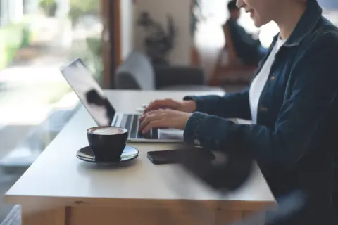 Kobieta pracuje zdalnie przy laptopie, popijając kawę. Nowy kodeks pracy reguluje takie formy zatrudnienia.