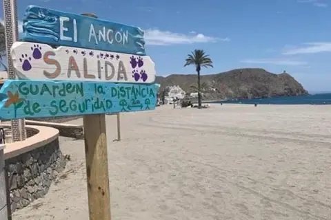 Cartel en la playa El Ancón, Carboneras: "Salida. Guarden la distancia de seguridad". Palmera y mar al fondo.