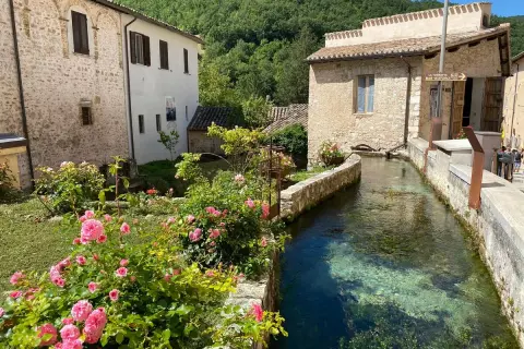 Un ruscello attraversa un borgo umbro, tra case in pietra e rose rosa. Un angolo incantevole tra i borghi più belli dell'Umbria.