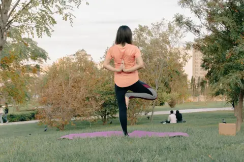 Mujer en postura de árbol, practicando yoga al aire libre en un parque.