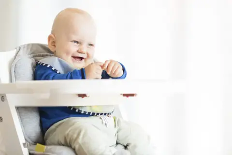 Uśmiechnięty niemowlak w krzesełku, gotowy na pyszny kefir dla niemowlaka.