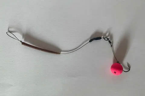 Ein **hinged stiff rig** mit einem pinken Pop-up Boilie und einem Haken.