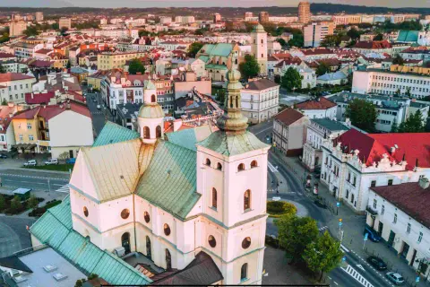 Widok z lotu ptaka na rzeszów rynek z dominującą białą bazyliką i zielonymi dachami. W tle zabudowa miejska.
