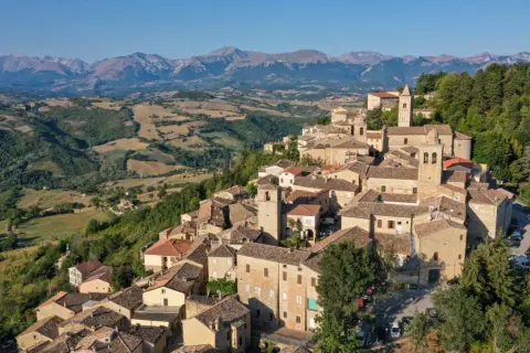 Borgo medievale di Penna San Giovanni, con le sue case in pietra e i tetti in cotto, incastonato tra dolci colline e montagne maestose.