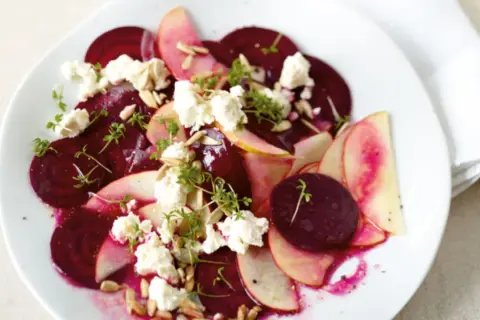 Ein köstlicher rote beete salat mit Apfelscheiben, zerbröckeltem Käse, Sonnenblumenkernen und Kresse garniert.
