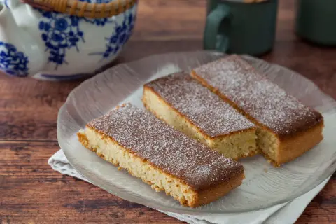 Saftiger mandelkuchen vom blech, bestäubt mit Puderzucker, auf einem Glas-Teller.