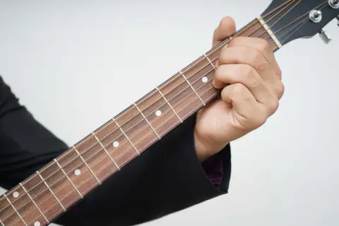 Dłoń dociska struny na gryfie gitary, rozpoczynając naukę gry na gitarze.