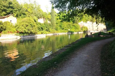 Sentiero lungo il canale, ideale per la ciclabile Peschiera Mantova. Vegetazione lussureggiante e riflessi sull'acqua.