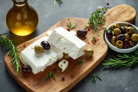 Kostki sera feta, oliwki, rozmaryn i oliwa z oliwek na desce. Idealne do sałatki, a feta kcal nie są tak wysokie.
