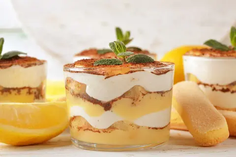 Délicieux tiramisu citron, superposé dans des verres avec des biscuits à la cuillère et des citrons frais.