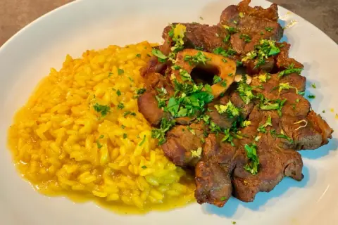 Ossobuco alla milanese succulento su un letto di risotto giallo brillante, guarnito con prezzemolo fresco.