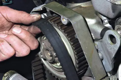 Dłoń mechanika sprawdza stan paska rozrządu przy kole zębatym silnika.