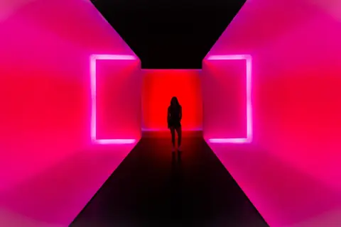 Kobieta stoi w korytarzu z neonowym oświetleniem. To nowoczesne instalacje artystyczne, które tworzą hipnotyzującą grę światła i koloru.