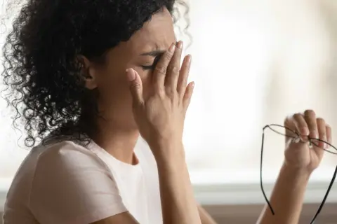 Frau reibt sich die Augen, hält Brille in der Hand. Sie fühlt sich erschöpft, vielleicht wegen **Schwindel durch Stress**.