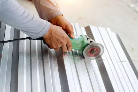 Ręce trzymają szlifierkę kątową, która tnie falistą blachę aluminiową wzdłuż czerwonej linii. To pokazuje, czym ciąć aluminium.
