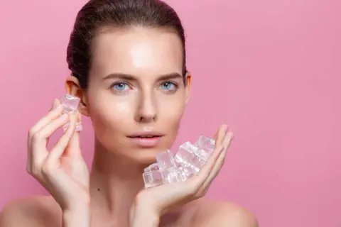 Une femme au visage frais tient des glaçons dans ses mains, un geste rafraîchissant pour la peau.