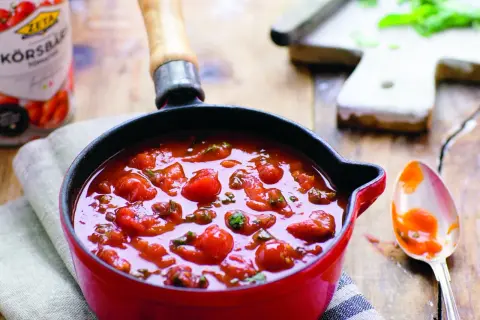 En röd gryta fylld med en hemlagad tomatsås, perfekt för ditt nästa tomatsås recept. En sked med sås ligger bredvid.