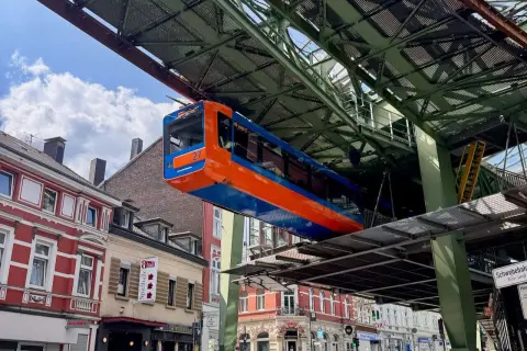 Die orange-blaue Schwebebahn fährt über den Dächern von Wuppertal.