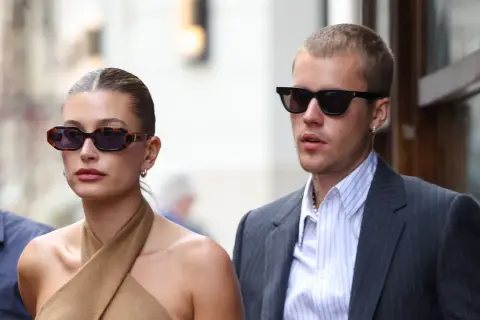 Hailey Bieber und Justin Bieber, beide mit Sonnenbrillen, wirken semi-formal. Sie spazieren durch die Stadt, sie in einem braunen Top, er im Anzug.