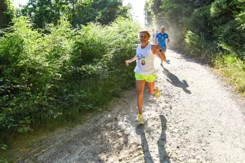 Donne e uomini corrono su un sentiero sterrato in un bosco, godendosi la corsa con il caldo estivo.