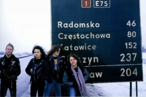 Czterech muzyków zespołu Metallica pozuje przy drogowskazie w Polsce. Może to zapowiedź ich koncertu Metallica Polska 2026?