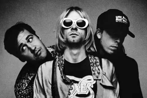 Drei Mitglieder von Grunge-Bands posieren für ein Schwarz-Weiß-Foto. Der Frontmann trägt auffällige weiße Sonnenbrillen.