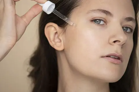 Una mano aplica un suero con gotero en la mejilla de una mujer. Descubre qué es el glutation y sus beneficios para la piel.