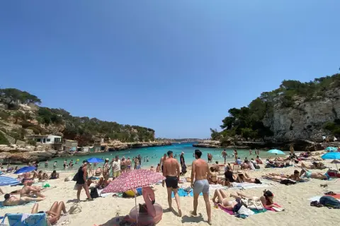 Majorka we wrześniu: słoneczna plaża pełna ludzi, turkusowa woda, skaliste wybrzeże. Idealna pogoda na wakacje.