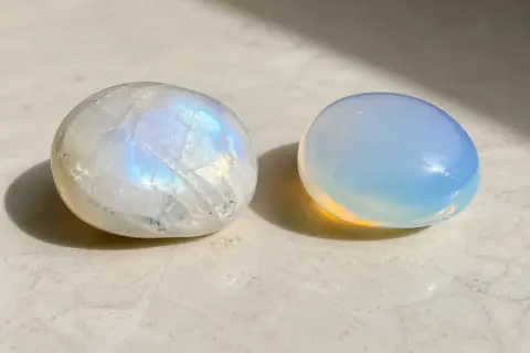 Dos piedras pulidas, una piedra luna iridiscente y otra de un azul lechoso, descansan sobre una superficie clara.