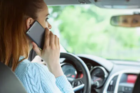 Kobieta rozmawia przez telefon podczas jazdy samochodem, ignorując drogę.