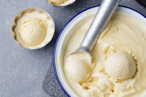 Krämig vaniljglass, perfekt för ett enkelt gelato recept. En skopa glass i en form och en stor skål med glass och skopa.
