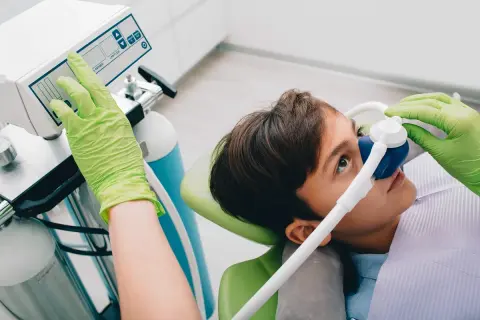 Chłopiec w masce z gazem rozweselającym, dentysta reguluje aparat.
