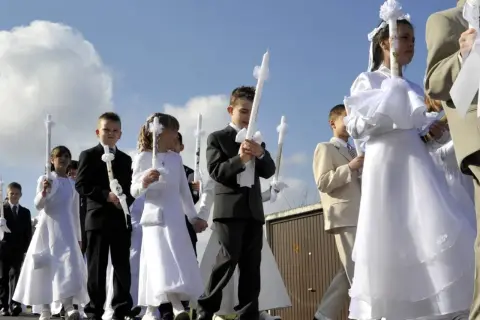 Kinder in festlicher Kleidung, oft weiße Kleider und Anzüge, tragen Kerzen zur Kommunion. Als Gast zur Kommunion zieht man sich festlich, aber dezent an.