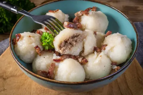 Pyzy ziemniaczane z mięsem, przygotowane według przepisu babci, podane w misce z chrupiącym boczkiem i natką pietruszki.
