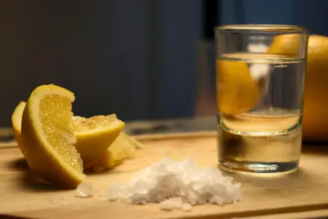 Składniki na vodka sour przepis: kieliszek wódki, cytryna i sól na desce.