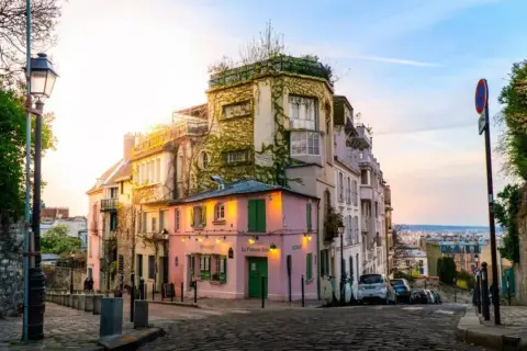 Ein malerisches Viertel in Paris, perfekt für einen Kurztrip. Ein rosa Restaurant mit grünen Fensterläden, umgeben von charmanten Häusern, lädt zum Verweilen ein.