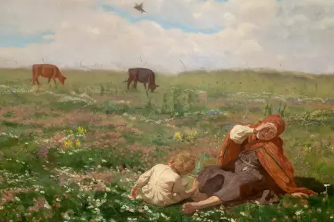 Obrazy wsi Chełmońskiego: kobieta z dzieckiem odpoczywa na kwiecistej łące, w tle pasą się krowy.