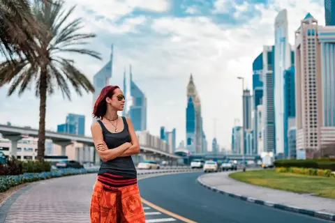 Turystka w Dubaju w pomarańczowej spódnicy i topie podziwia panoramę miasta.