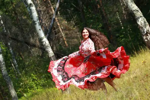 Una giovane donna con lunghi capelli scuri, vestita con un abito rosso svolazzante, danza in un bosco. Sembra una delle giostrai Sinti, piena di gioia e vitalità.