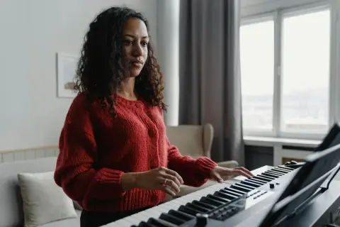 Kobieta w czerwonym swetrze ćwiczy grę na pianinie, ucząc się nowych melodii.