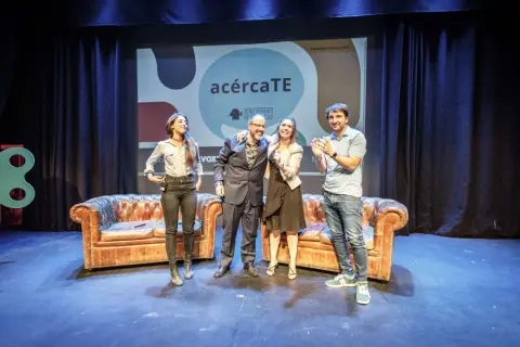 Cuatro personas celebran en un escenario con sofás y un cartel de "acércaTE". Un evento de podcast psicologia.