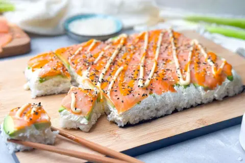 Rechteckige sushi rollen ohne matte, belegt mit Lachs, Avocado und Mayonnaise, bestreut mit Sesam.