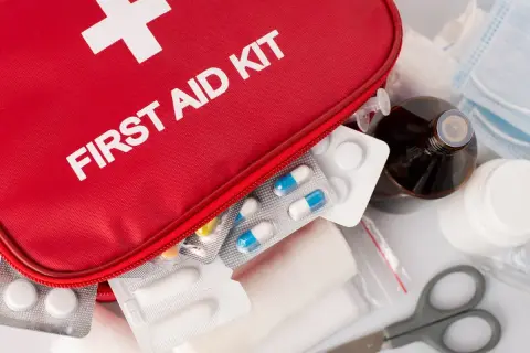 Czerwona apteczka z napisem "FIRST AID KIT", tabletki, bandaże, buteleczka z płynem i maski.